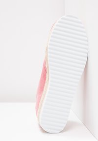 Chaussure en suède rose avec une semelle blanche en caoutchouc. La semelle présente un motif strié, et un accent en jute texturé est visible à la base.