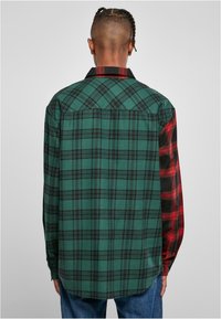 Groene en zwarte geruite flanellen shirt met een rode geruite accent op de rechtermouw, met knoopmanchetten en een puntige kraag.
