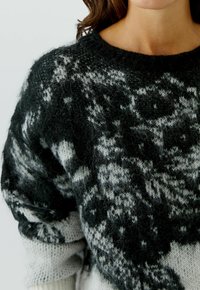 Schwarzer und weiß gemusterter Pullover mit lockerer Passform, Rundhalsausschnitt und strukturiertem Strickmaterial, das verschiedene Farbtöne und weiche Fasern aufweist.