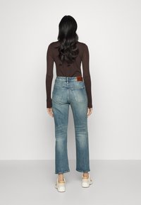 Bakifrån av en person som bär ljusblå denimjeans med utvikta ben, som kombineras med en brun långärmad tröja och vita sneakers.