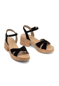Czarne zamszowe sandały z masywną, strukturalną podeszwą, wyposażone w krzyżujące się paski i zapięcie na kostce, zapewniające stabilne dopasowanie i wsparcie.