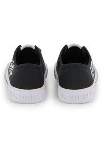 Μαύρα πάνινα παπούτσια με λευκή καουτσούκ σόλα, με έντονο λογότυπο στη φτέρνα και χαμηλή σχεδίαση. Δεν έχουν κορδόνια ή εμφανείς κλειδαριές.