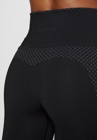 Leggings negros de cintura alta hechos de tela texturizada, con un acabado mate y un patrón de puntos tonales en la cinturilla y la parte alta del muslo.