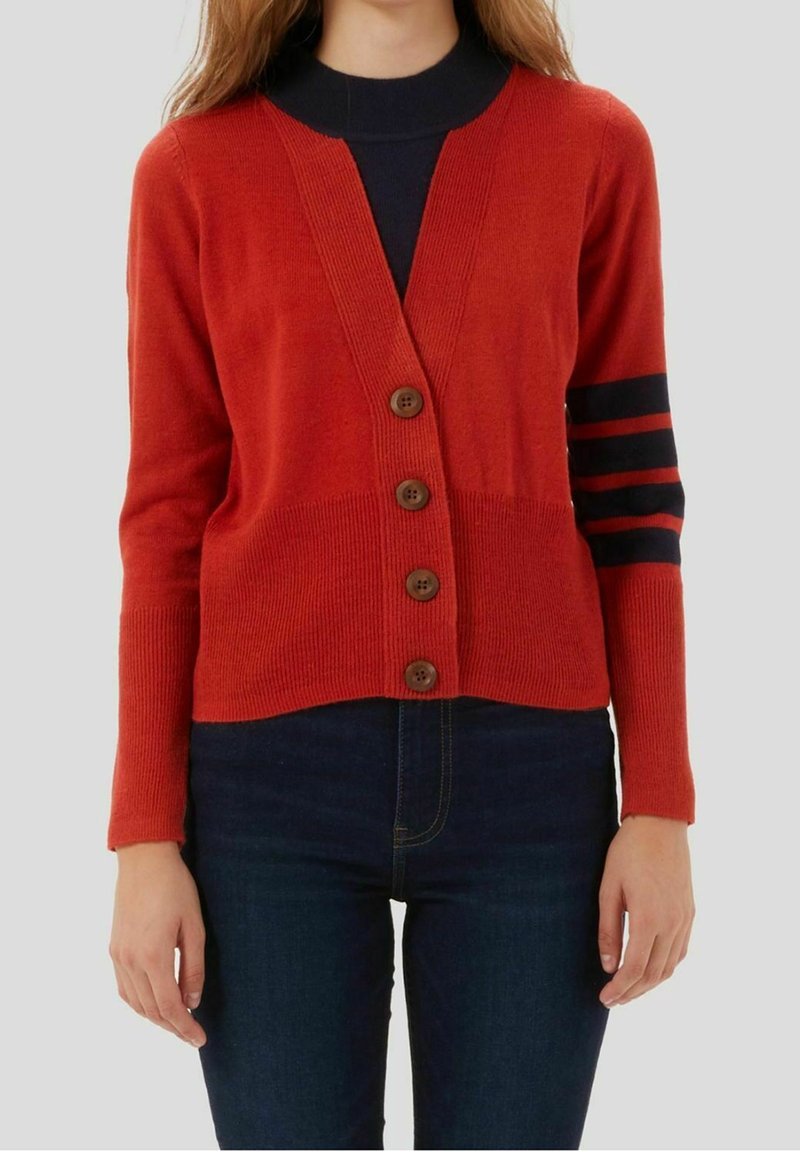 Red knitted cardigan with a V-neck, five brown buttons, and navy horizontal stripes on the sleeves. Worn over a black top.