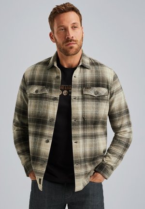 Geruite flanellen shirt in beige en zwart tinten met knoopsluiting aan de voorkant, twee borstzakken en een kraag. Draagt over een zwart graphic t-shirt.