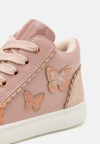 Rosa syntetisk sneaker med sommerfugl-applikasjoner, en glansfull rosa hæltab og en glitrende bakpanel med teksturerte detaljer.