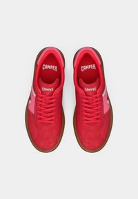 Een paar rode en roze sneakers van het merk Camper met bruine zolen, gezien van bovenaf op een witte achtergrond.