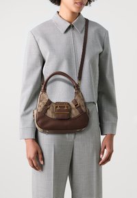 Bolsa de pele castanha e tecido estampado com uma silhueta curva, ferragens douradas e uma alça de ombro destacável. Exibida num modelo.