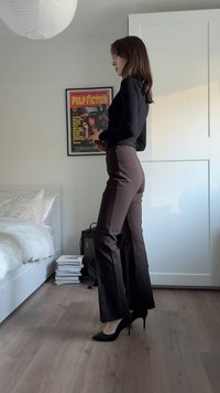 Pantalon marron taille haute en tissu lisse, associé à des escarpins noirs et un haut noir à manches longues ajusté.