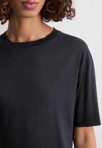 Schwarzes Baumwoll-T-Shirt mit Rundhalsausschnitt und kurzen Ärmeln. Verfügt über eine glatte Textur und einen gerippten Kragen für zusätzlichen Detail.