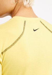 Żółta koszulka Nike z czarnym logo i kontrastującymi szwami na ramionach i kołnierzu dla dodatkowych detali. Miękka faktura materiału.