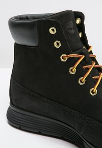 Stivale alla caviglia in suede nero con colletto imbottito, lacci gialli e rossi e occhielli in metallo dorato. Suola in gomma per durata e trazione.