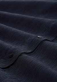Marine textiel met een golvend patroon en zwarte knopen, dat een zachte, gelaagde uitstraling toont met horizontale ribbels.