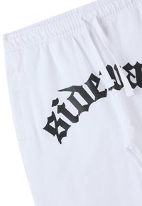 Pantaloni della tuta bianchi con un elastico in vita, grafica in lettere gotiche nere che recita "Side" e tasche laterali per funzionalità.