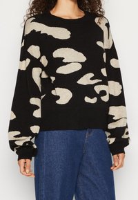 Schwarzer Strickpullover mit abstrakten beigen Mustern. Verfügt über einen runden Halsausschnitt, lange Ärmel und gerippte Bündchen. Weiche Textur und lockerer Schnitt.