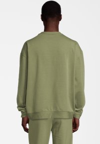 Sudadera verde de corte relajado, con puños y dobladillo acanalados. Fabricada en una tela suave con una textura lisa y sin logotipos ni patrones visibles.