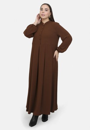 Long brown dress made of textured fabric, featuring a high neckline, button closures, and pleated skirt. Paired with black heeled boots.