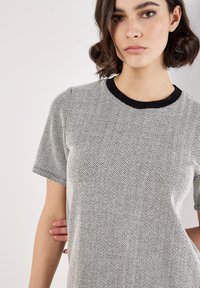 T-shirt z krótkim rękawem w czarno-białym wzorze w jodełkę, z czarną prążkowaną dekoltem i miękką, teksturowaną tkaniną.