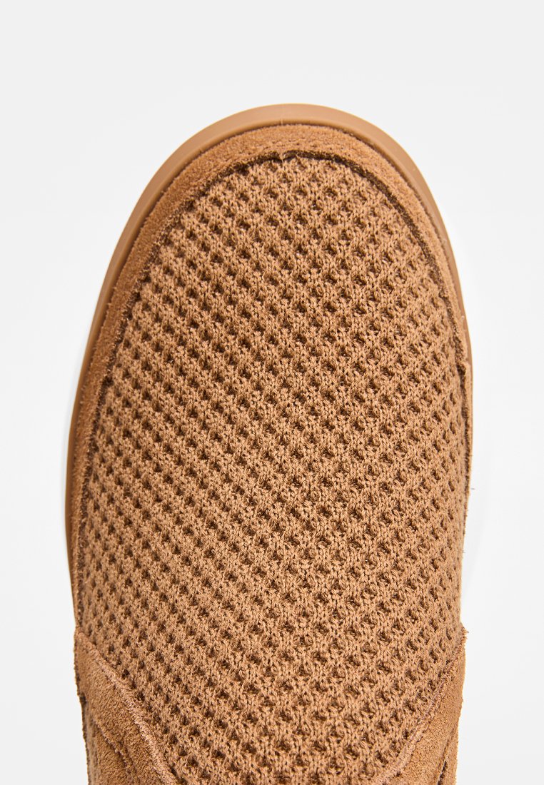 Chaussure en mesh marron à enfiler avec une surface texturée, un bout arrondi et une semelle flexible. Présente un renforcement lisse le long du bord.