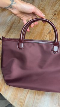 Borsa sintetica color mogano con texture liscia, manici arrotondati e chiusura con zip. Presenta dettagli angolari in pelle e un design spazioso.