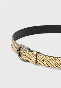 Kultainen teksturoitu nahkavyö mustalla ristikkokuvioinnilla ja tummalla metallisoljella yksinkertaista taustaa vasten.