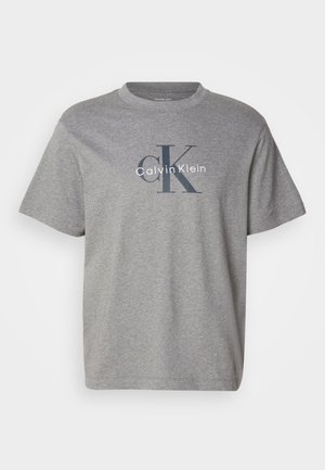 Szary t-shirt z krótkim rękawem i okrągłym dekoltem z dużym logo "cK" i "Calvin Klein" nadrukowanym na piersi w ciemnym i białym kolorze.