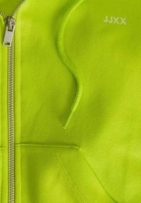 Neonově zelená mikina na zip s hladkým povrchem, s kovovým zipem a malou potisknutou etiketou "JJXX" na pravém horním rohu.