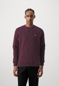 Bordo spalvos megztinis ilgomis rankovėmis, apvaliu kaklu ir veliūrinėmis rankogaliais. Yra mažas geltonas logotipas kairėje krūtinės pusėje.