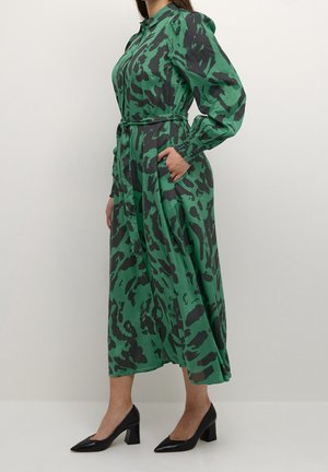 Robe chemise à manches longues avec ceinture à la taille, à motifs verts et noirs, en tissu léger, dotée de poches latérales et d'une silhouette fluide.