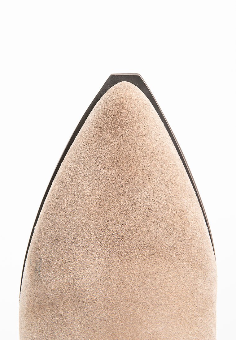 Zapato de ante beige con punta afilada y suela negra elegante. La parte superior presenta una textura suave y una punta bien definida.