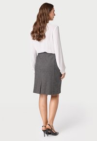 Grijze getailleerde kokerrok met een achterkant split, gecombineerd met een witte lange mouwen blouse. Model draagt zwarte hakken.