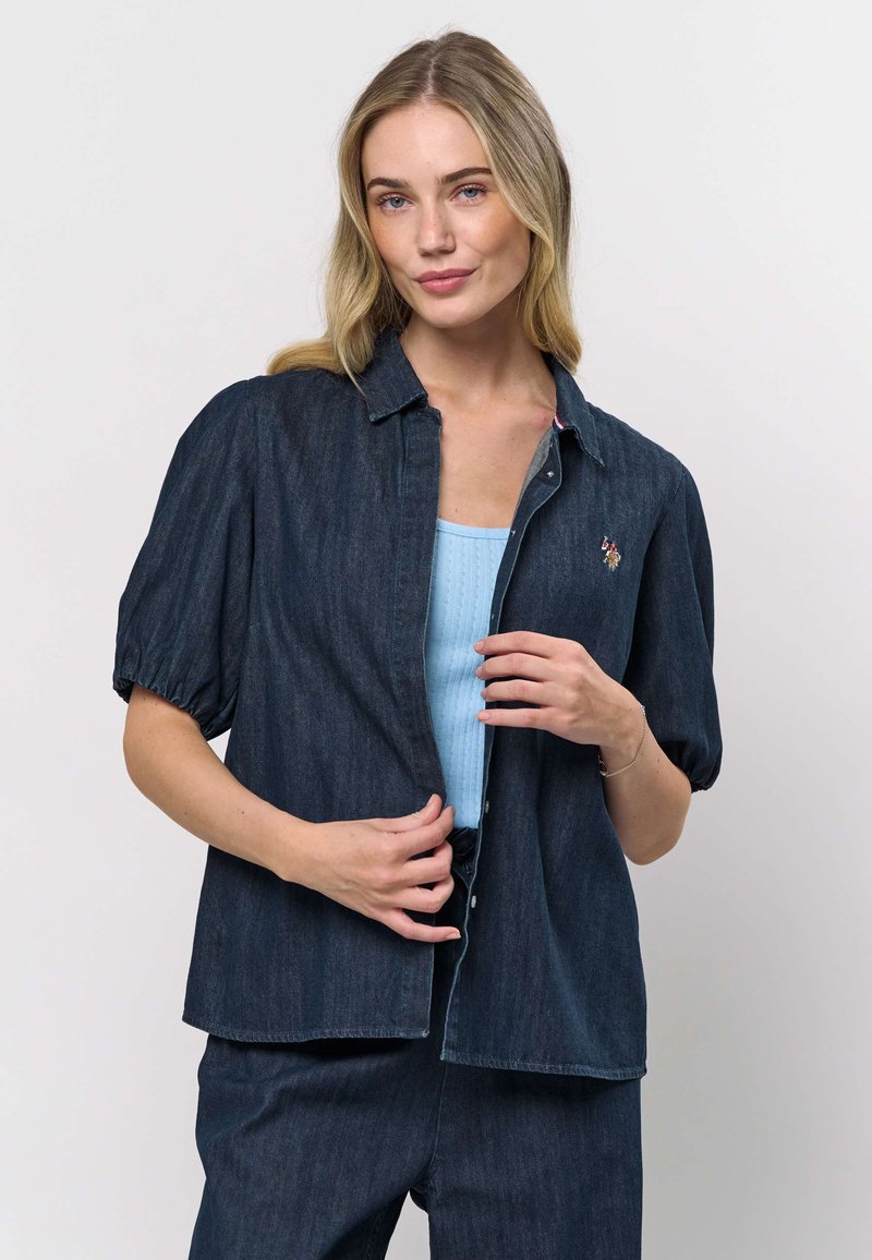 Denim overhemd met korte mouwen, met knoopsluiting aan de voorkant, donkerblauwe kleur en subtiele patroonstructuur. Heeft een geborduurd ontwerp op de borst.