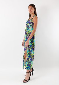 Färgglad mönstrad klänning med en blandning av grönt, blått, gult och lila, med en djup V-ringning och höga sidoklyftor. Bärs med svarta klackar.
