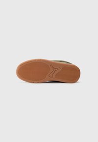 Sål af sko med brunt gummigreb, Puma-logo i midten og teksten "SEES VI I PARKEN" præget nær hælen.