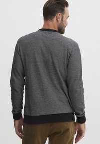 Suéter gris a rayas con mangas largas y un cuello en canalé azul marino y dobladillo inferior. La textura parece suave y tejida, con un ajuste relajado.