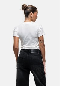 Witte T-shirt met korte mouwen gecombineerd met hoogwaist zwarte denim jeans. De jeans hebben een gestructureerde stof en zakken aan de achterkant.
