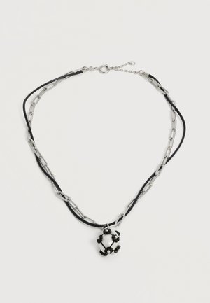 Collier à double couche avec chaîne en argent et cordons noirs, présentant un pendentif sphérique blanc orné de petites perles noires et nacrées.