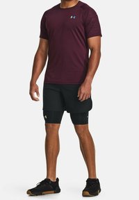Camiseta deportiva de manga corta en color marrón con pantalones cortos negros. Ambos cuentan con una tela transpirable; la camiseta tiene un logo y acentos texturizados en los hombros.