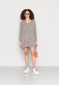 Vestido floral de manga longa com decote em V, base preta, flores brancas e bege, combinado com ténis brancos e uma bolsa laranja.