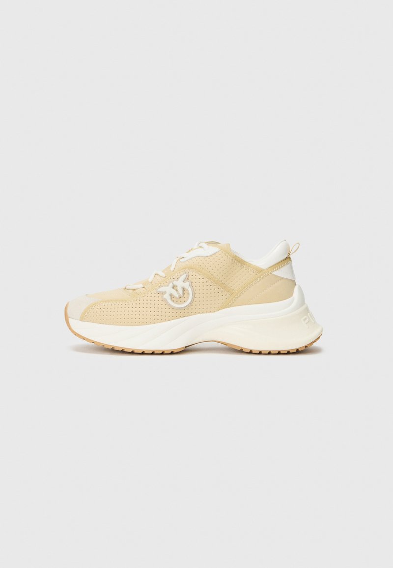 Baskets de sport beige clair avec un dessus perforé, accents blancs et semelle incurvée. Présente un logo sur le côté et des lacets pour un maintien sécurisé.