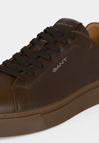 Baskets GANT en cuir marron avec lacets noirs, semelle cousue et nom de la marque imprimé sur la languette et le côté du chaussure.