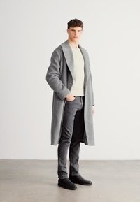 Γκρι μάλλινο παλτό με γιακά σάλι, φορεμένο πάνω από ένα ανοιχτόχρωμο πουλόβερ, συνδυασμένο με σκούρα τζιν και μαύρα παπούτσια. Λεπτό ύφασμα, ραμμένο κατά παραγγελία.