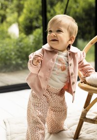 Helles rosa Jacket mit Knopfleiste, weißes Shirt mit einem Seepferdchen-Motiv und Blumenmuster-Hosen in sanftem Orange und Weiß.