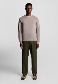 Lichtbruine sweatshirt met witte kraagtrim, gecombineerd met donkere groene broeken. Bruin en beige gestreepte sneakers maken de outfit compleet.