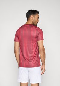 Rood atletisch T-shirt met een gestreept patroon en korte mouwen, gemaakt van gladde stof, gedragen met witte korte broek.