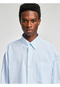 Lyseblå stripete skjorte laget av lett stoff, med button-down-krage, brystlomme og avslappet passform med senkede skuldre.