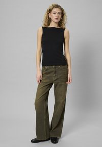 Top senza maniche nero, dal design aderente. Jeans a gamba larga verde oliva con una texture sbiadita e stile a cinque tasche. Scarpe nere completano l'outfit.