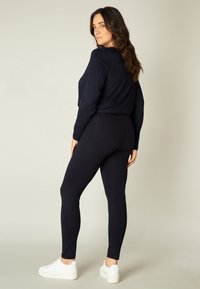 Marineblauwe tweedelige outfit gemaakt van zachte, rekbare stof. Bevat een aansluitende cropped top en taps toelopende leggings, gecombineerd met witte sneakers.