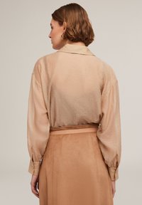 Beige doorschijnende blouse met kleine metalen stippen, lange mouwen en een kraag, gecombineerd met een bijpassende zachte tan suède rok.