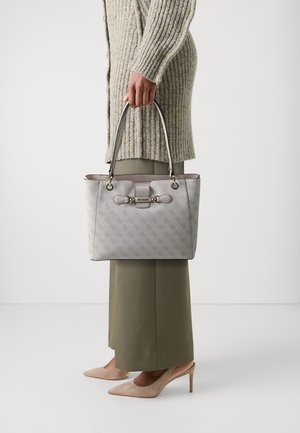 Sac à main gris à motifs avec deux anses supérieures, comportant des éléments en or et un détail de fermoir. Porté avec un pantalon couleur olive et des talons beiges.